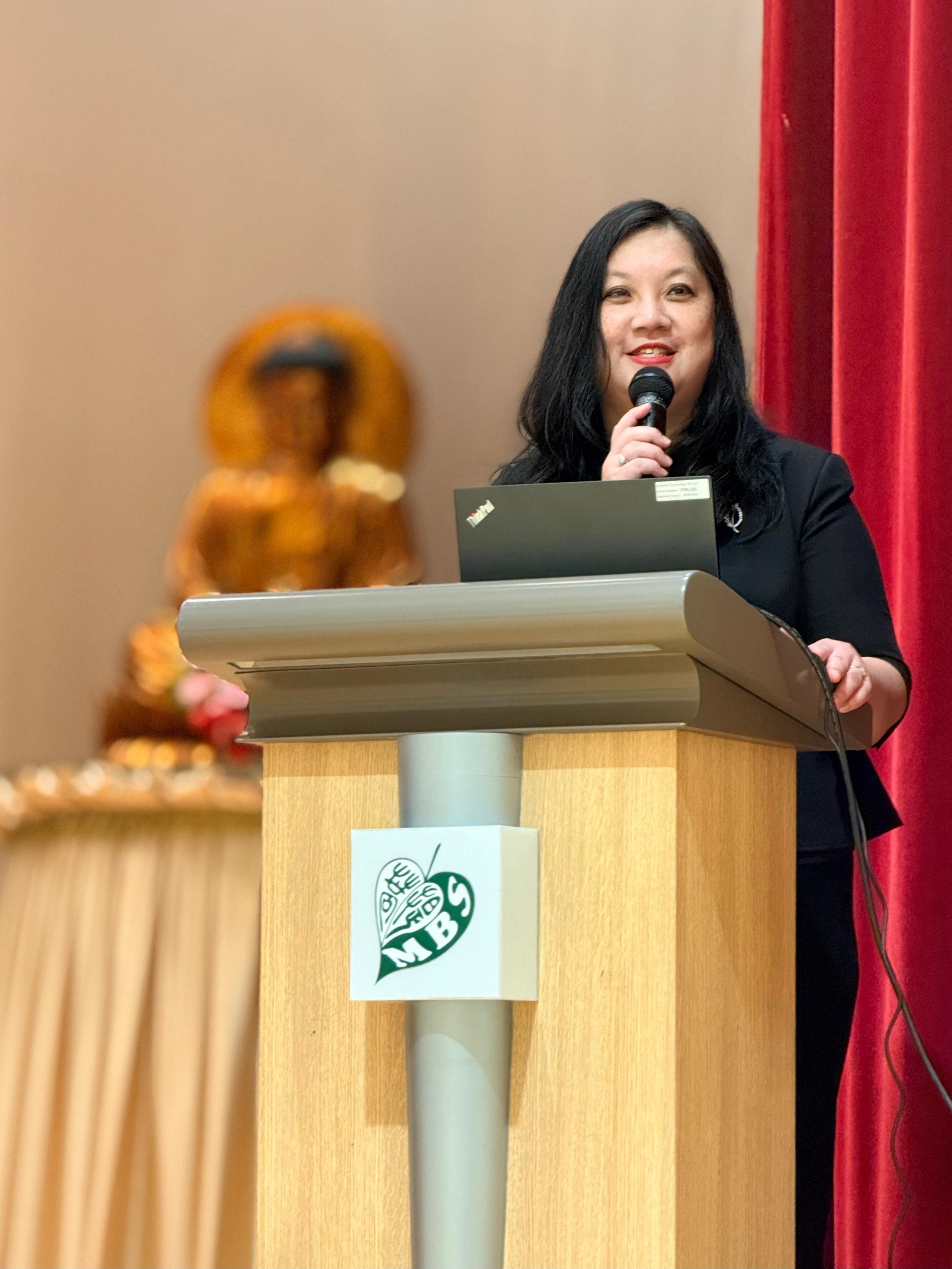 Principal Mrs See Lai Kwan addressing P6 pupils on hall stage standing behind the rostrum during 22nd OPAC